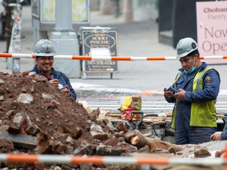 Two constuction workers standing inside a hole they just dug.